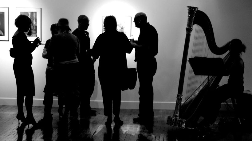 art gallery otvaranje, grupa ljudi razgovara uz muziku harfe u galeriji